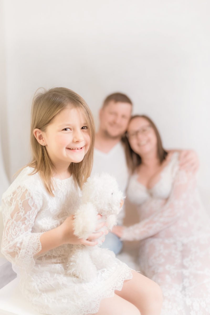 kind im vordergrund und werdende eltern im hintergrund fotografiert