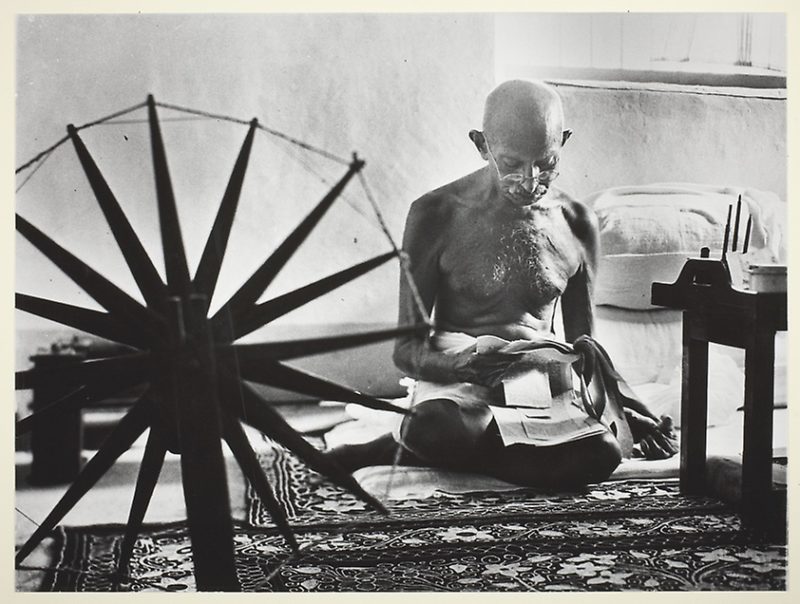 gandhi sitzt auf dem boden vor einem spinnrad