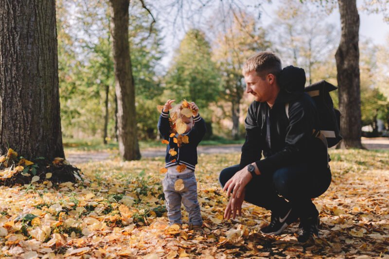 familienfotos im wald mit kind und vater spielend mit blaetter auf dem boden