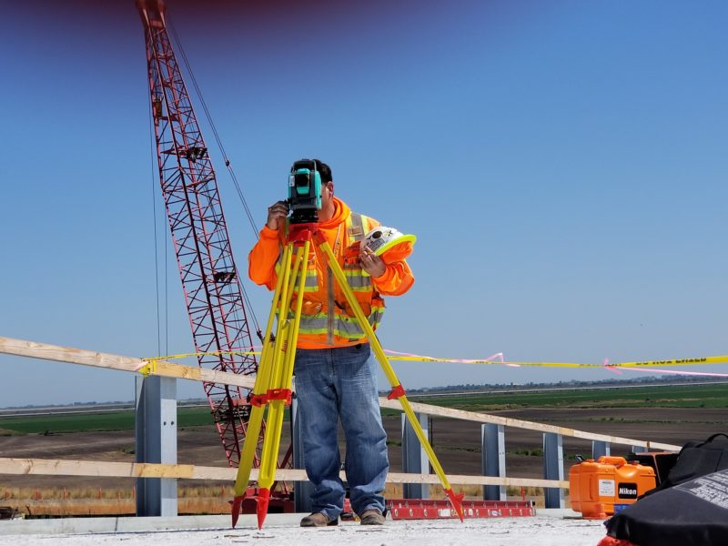 mann auf baustelle macht fotos mit kamera auf stativ