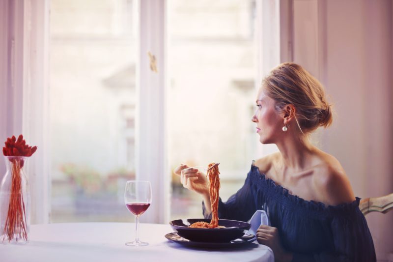 frau isst spaghetti vor dem fenster am tisch