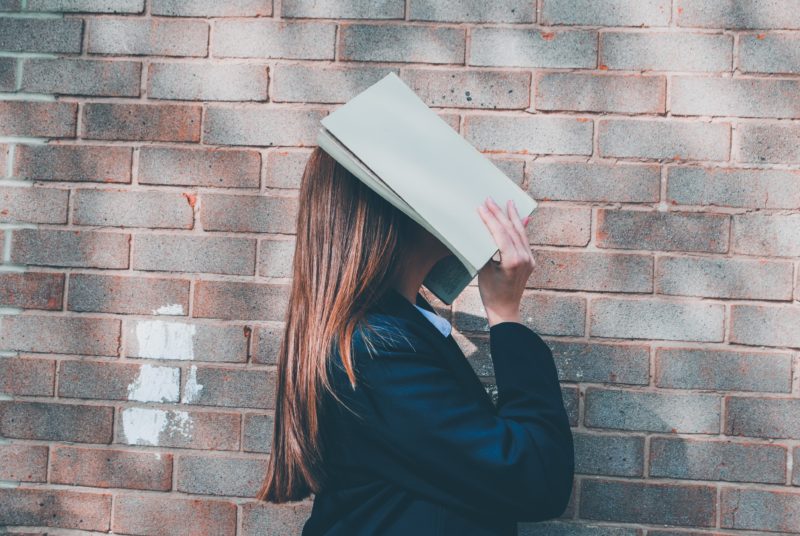 frau versteckt ihr gesicht mit einem buch