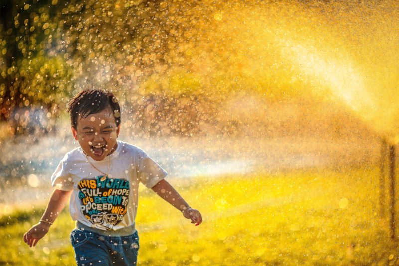 inszenierte fotografie: kleiner junge rennt durch sprinkleranlage