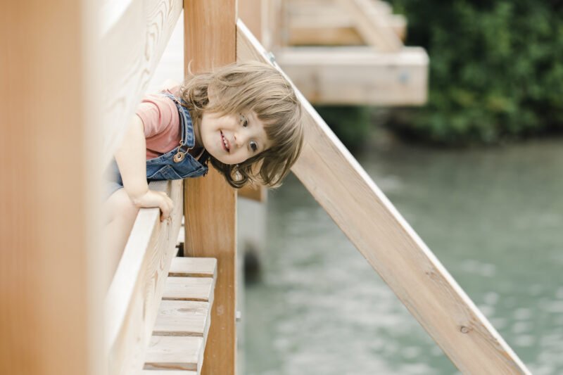 kleines maedchen laechelt durch holzbruecke am wasser