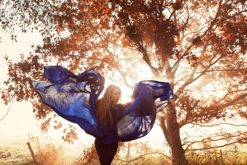 frau mit blauem tuch vor einem baum posierend