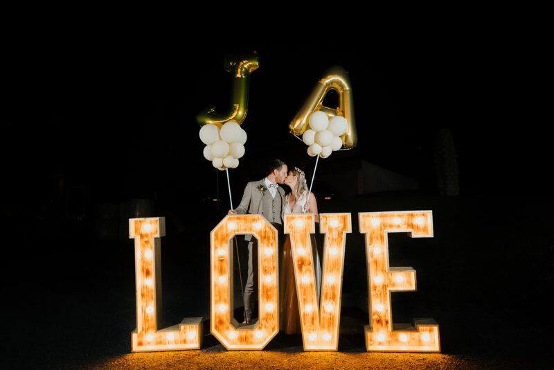 brautpaar kuesst sich vor grossem love schild in der nacht